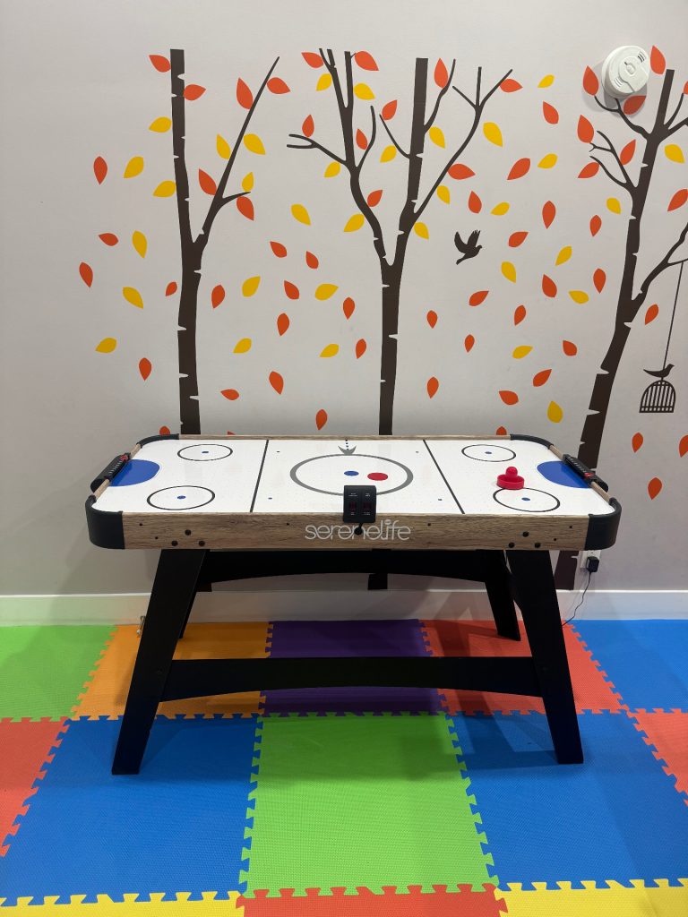 Air hockey table on rainbow foam flooring with autumn tree mural